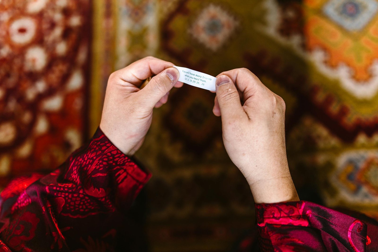 Hands holding a fortune cookie message over a colorful detailed carpet background.